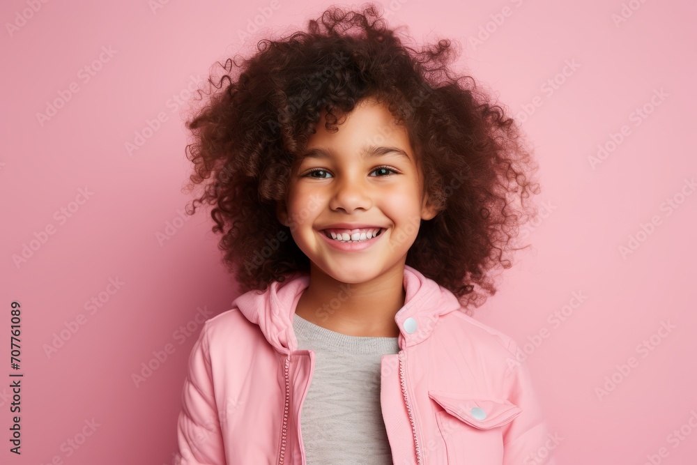 Portrait of cute african american little girl with curly hair in pink jacket on pink background Portrait of cute african american little girl with curly hair in pink jacket on pink background