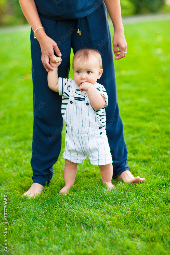 Baby learning to walk outdoors. Happy mother and her son playing in park together Baby learning to walk outdoors. Happy mother and her son playing in park together