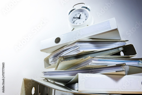 Alarm clock on stacked ring binders against a gray background threatened to deadline ultimatum, business concept for time management and work overload, view from below, copy space photo