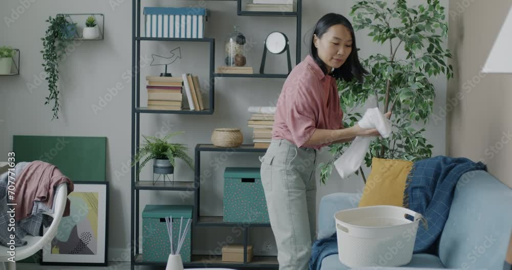 Cheerful Asian woman collecting dirty clothes into basket doing laundry cleaning apartment smiling. Home and domestic chores concept. Cheerful Asian woman collecting dirty clothes into basket doing laundry cleaning apartment smiling. Home and domestic chores concept.