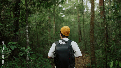 A man backpacker traveling alone in forest wild. Young man hiking trip through the green forest with backpacks. Asian man traveler explore while walking in green forest. Travel and backpack concept