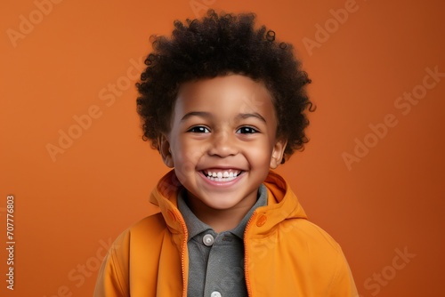 a professional portrait studio photo of a cute black boy child model with perfect clean teeth laughing and smiling. isolated on orange background. for ads and web design © JAYDESIGNZ