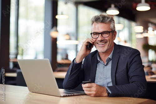 Smiling young businessman talking on the phone using laptop at work. Happy