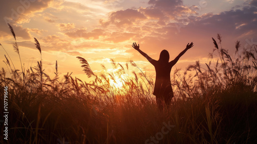 Silhouette photo of one woman standing in outdoor grasses field raising two hands in the air showing freedom relax emotion at twilight time with beautiful sunset.
