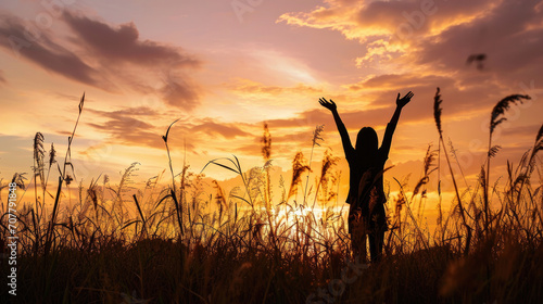 Silhouette photo of one woman standing in outdoor grasses field raising two hands in the air showing freedom relax emotion at twilight time with beautiful sunset. #707791848