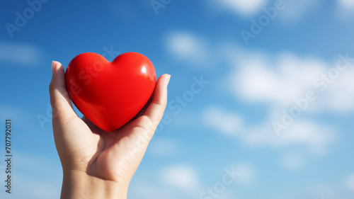 Hand holding red heart shape on sky background