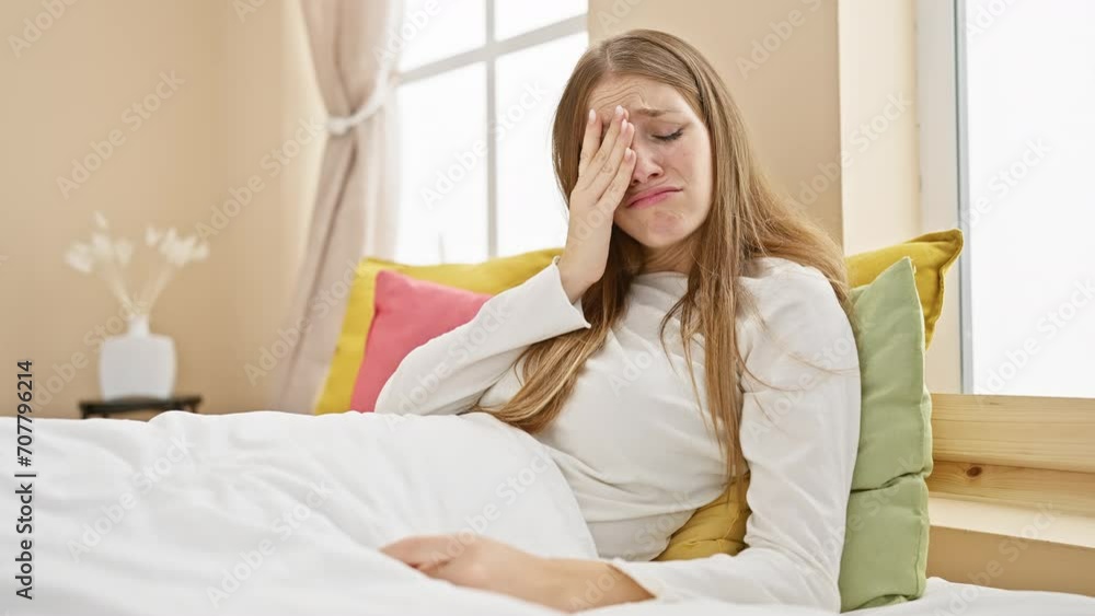 Exhausted young blonde woman in pyjama covering half face with hand, yawning in fatigue - intimate indoor portrait of sleep-deprived female sitting in bed grapples with morning boredom Exhausted young blonde woman in pyjama covering half face with hand, yawning in fatigue - intimate indoor portrait of sleep-deprived female sitting in bed grapples with morning boredom