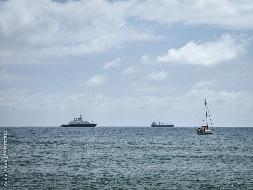 A luxury yacht, a container ship and a sailboat on the sea horizon on the Mediterranean Sea off the coast of Málaga, Spain
