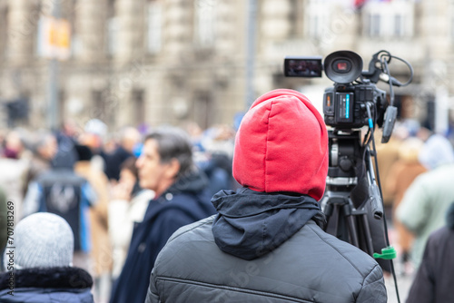 Filming crowd of people at street during winter day, television camera operator in the focus