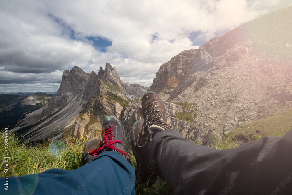 Trekking boots of a hiker couple while sitting on top of a mountain in Seceda, Dolomites, Italy