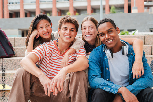 Portrait of a group of real multiracial high school students smiling and looking at camera sitting on the steps of a university campus stairway. International teenage friends laughing. Young people