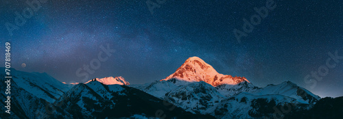 Obraz na płótnie Stepantsminda, Gergeti, Georgia. Mount Kazbek Covered Snow In Winter Sunrise. Morning Dawn Colored Top Of Mountain In Pink-orange Colors. Awesome Winter Georgian Nature Landscape. night sky, night w salonie