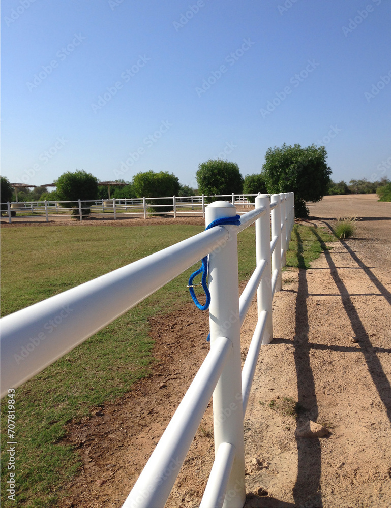 White rail fence on grass bank against blue sky White rail fence on grass bank against blue sky