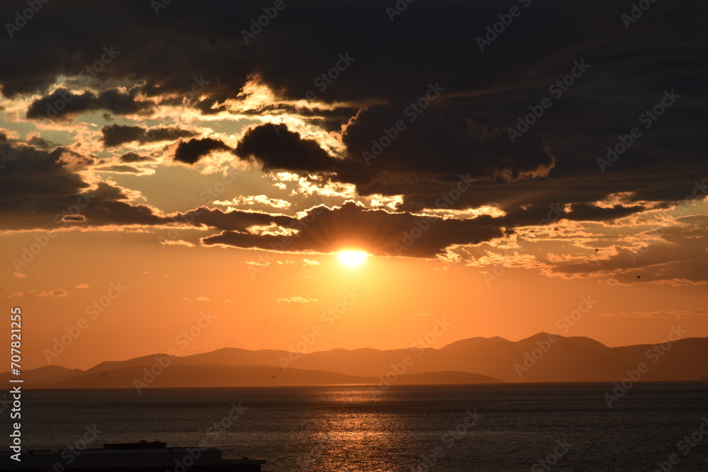 Naklejka premium Dramatic Sunset Over the Ocean with Clouds and Mountains Silhouette