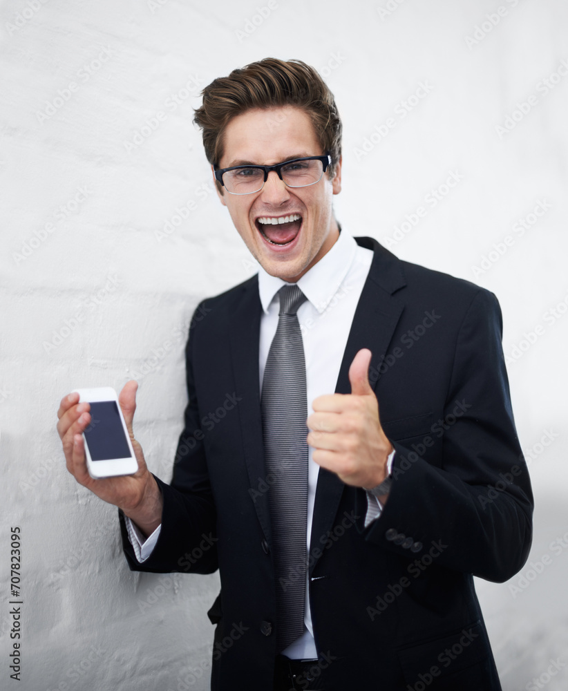 Excited businessman, portrait and phone with thumbs up for success against a gray wall background. Happy man or employee smile with mobile smartphone, like emoji or yes sign for winning or good job Excited businessman, portrait and phone with thumbs up for success against a gray wall background. Happy man or employee smile with mobile smartphone, like emoji or yes sign for winning or good job