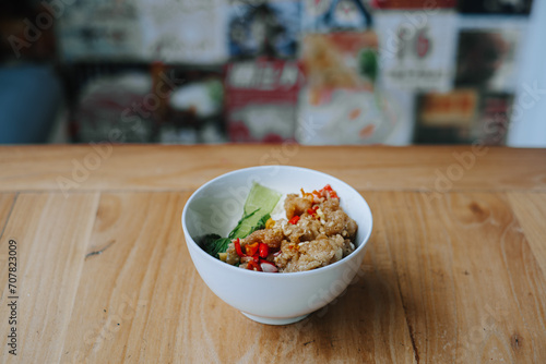 A bowl of Salt Chili Chicken known as Ayam Cabe Garam in Indonesia with rice and vegetables on wooden table. Bokeh background. photo