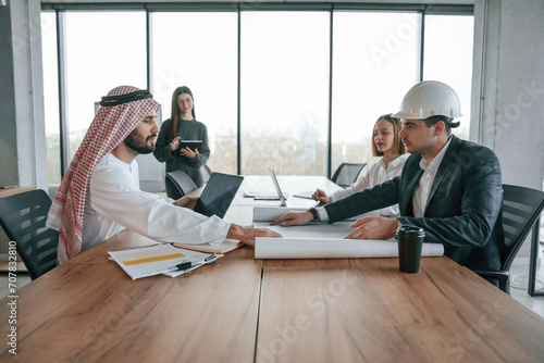 Working with a plan. Muslim businessman in traditional outfit with colleagues in office