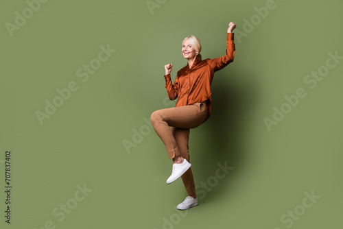 Full size photo of pretty retired female celebrate raise fists promo dressed stylish silk brown outfit isolated on khaki color background