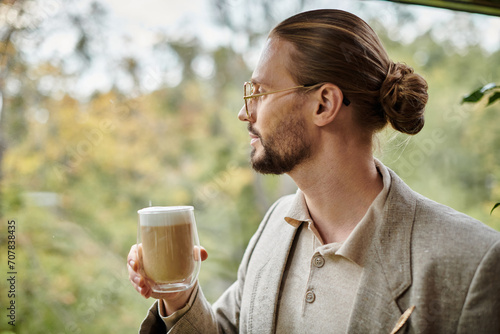 handsome appealing man with beard and collected hair in elegant suit drinking his hot coffee photo