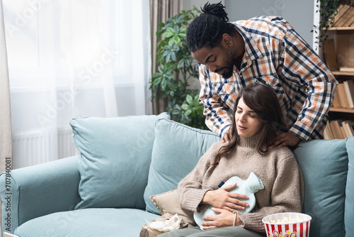 Mixed race couple African American man and white woman, male massage his girlfriend or wife in her menstrual period while sitting at home. Love, support and respect in relationship or marriage concept photo