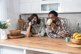 Young couple drinking coffee together in the kitchen on early morning before they go to the work. Emotional people spending free time with tea and conversation.