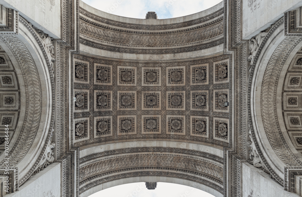 Looking up at the centre of the famous Arc de Triomphe. Detail under view of carvings under the arch of the Triumphal Arch. Iconic touristic architectural landmark of Paris, Selective focus.