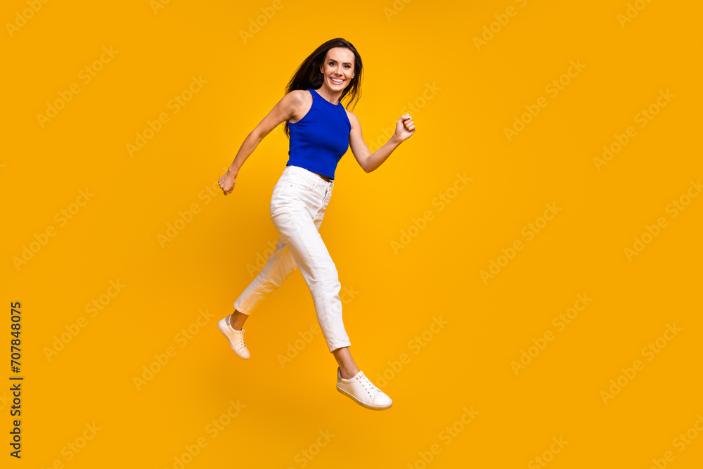 Full length photo of adorable pretty lady dressed blue top jumping hurrying empty space isolated yellow color background