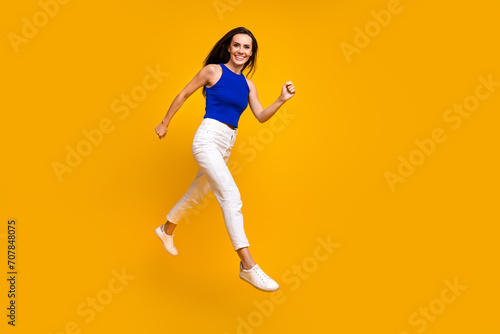 Full length photo of adorable pretty lady dressed blue top jumping hurrying empty space isolated yellow color background