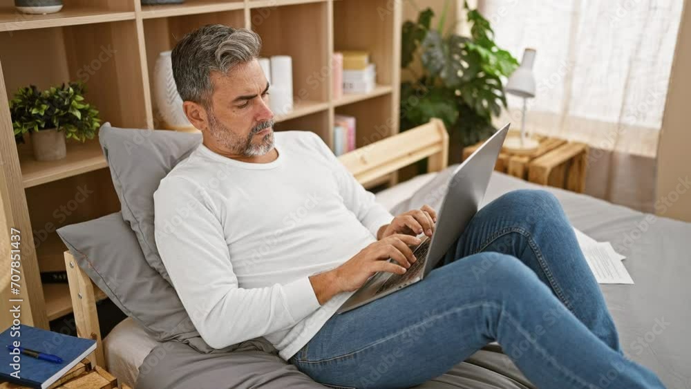 Young hispanic grey-haired man using laptop lying on bed at bedroom Young hispanic grey-haired man using laptop lying on bed at bedroom