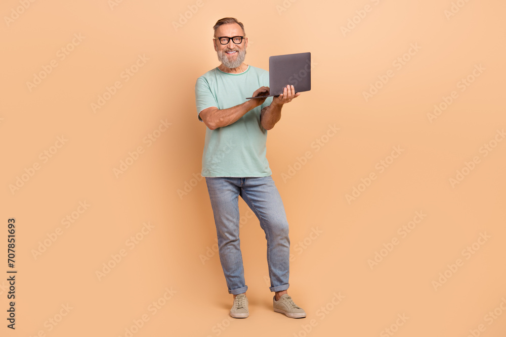 Full size photo of positive aged man hold use laptop coworking empty space isolated on beige color background Full size photo of positive aged man hold use laptop coworking empty space isolated on beige color background