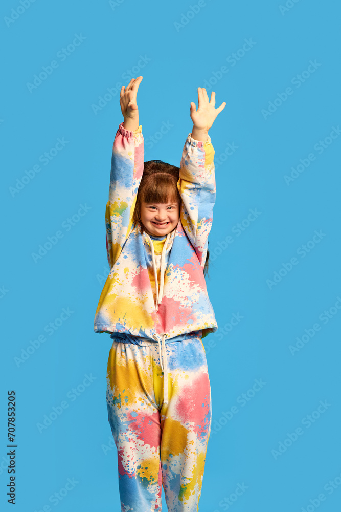 Smiling girl with down syndrome expressing happiness and joy against blue studio background. Tolerance, support and care. Concept of acceptance, inclusion, health, diversity, emotions Smiling girl with down syndrome expressing happiness and joy against blue studio background. Tolerance, support and care. Concept of acceptance, inclusion, health, diversity, emotions