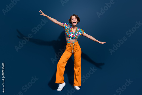 Full size photo of attractive young woman hands wings play fight wear trendy flared pants clothes isolated on dark blue color background