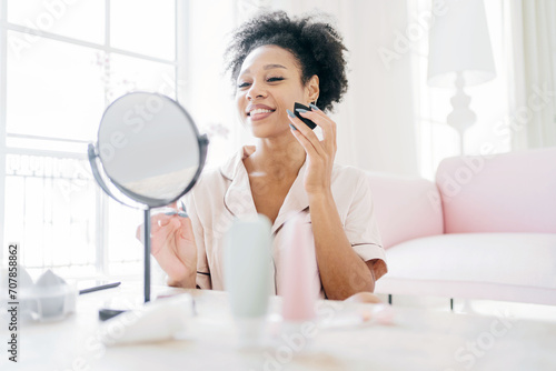 Radiant woman applying makeup with a brush, enjoying her beauty routine.