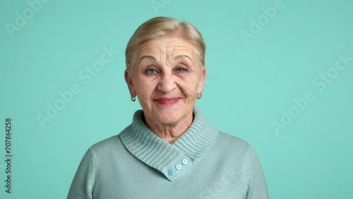 Positive tidy lady of 60-70 years with short blonde hair wearing blue sweater standing over blue background supporting somebody, agreeing with someone. High quality 4k footage photo