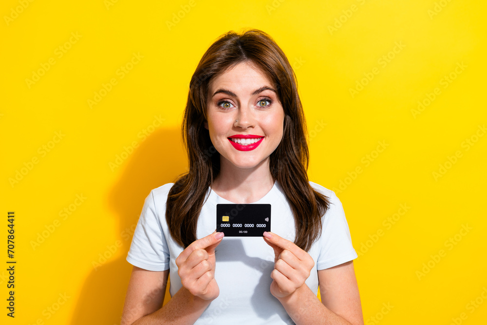 Photo of toothy beaming smart woman with brunette hair dressed white t-shirt hands hold credit card isolated on yellow color background Photo of toothy beaming smart woman with brunette hair dressed white t-shirt hands hold credit card isolated on yellow color background
