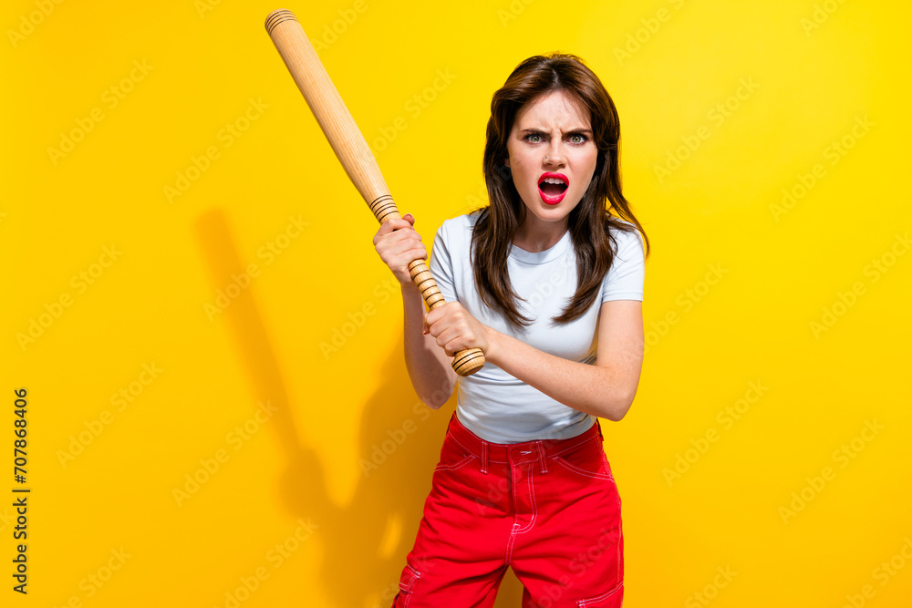 Portrait of angry aggressive girl with retro hairdo wear white t-shirt threatens you with baseball bat isolated on yellow color background Portrait of angry aggressive girl with retro hairdo wear white t-shirt threatens you with baseball bat isolated on yellow color background