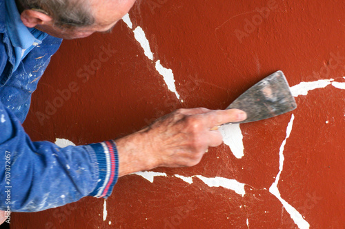 bricklayer mason painter worker  removing peeling paint on  wall with a spatula to later paint photo