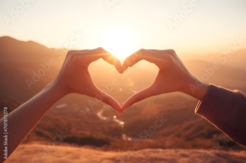 A close-up of a couple's hands forming a heart shape together against a scenic backdrop.