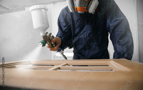 Professional worker staining wood furniture with spray gun