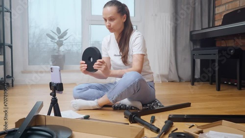 A vlogger girl shoots DIY video content with an overview of parts for self-assembly of furniture on a phone camera mounted on a tripod for subscribers of her channel. photo