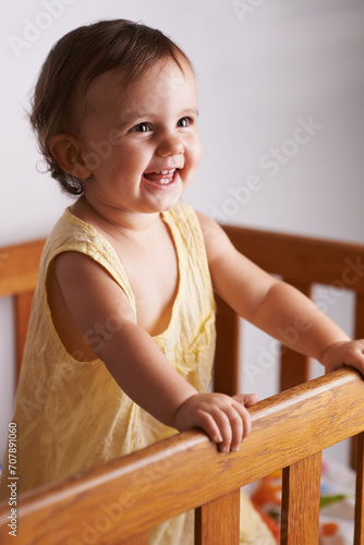 Cute, laughing and a child in a crib for playing, wake up or comfort in a bedroom. Happy, baby and a young kid in a nursery or room for thinking, idea or innocent standing for development in a home