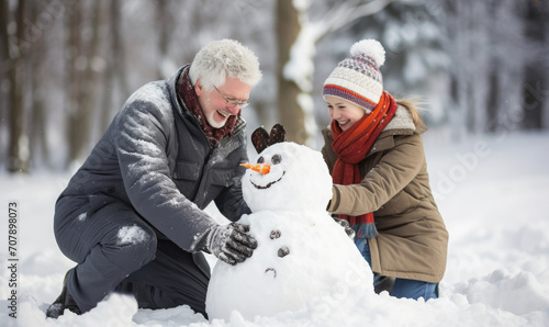Granddad and child building a snowman outside. Winter holiday family activity 