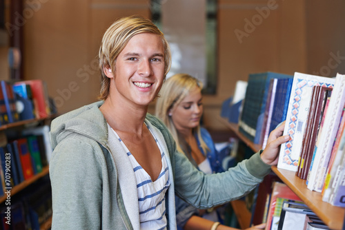 Portrait, book or happy man in library to search at university, college or school campus for education. Bookshelf, learning or student with scholarship studying knowledge, research and information