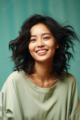 Smiling young asian woman with flying hair over green curtain background