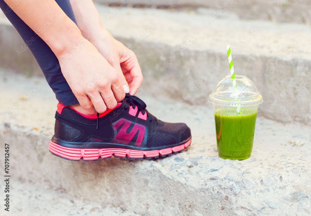 Green detox smoothie cup and woman lacing running shoes before workout