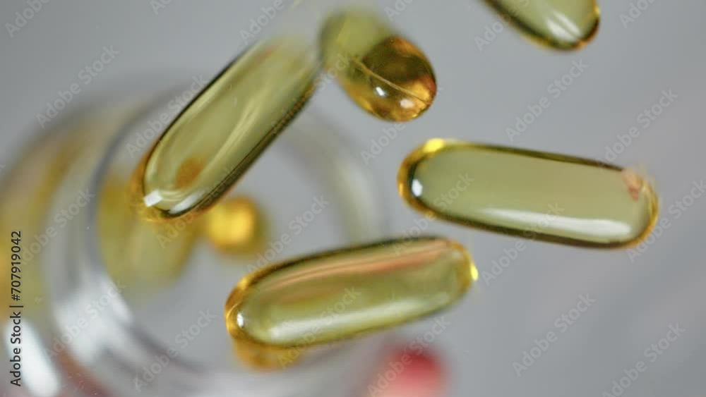 Close up shot hand pouring omega 3 fish oil capsules vitamine D3 vitamin E capsules on flat surface from a bottle Close up shot hand pouring omega 3 fish oil capsules vitamine D3 vitamin E capsules on flat surface from a bottle