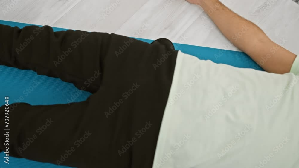 Bearded young man in casual attire lying on a blue yoga mat indoors for relaxation or exercise Bearded young man in casual attire lying on a blue yoga mat indoors for relaxation or exercise