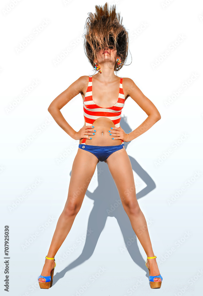 Fashionable young slim sexy woman with flying long hair in stylish swimsuit, posing against white background
