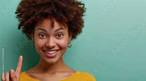 Cheerful afro black young woman, pointing with the finger, isolated on plain green background. photo