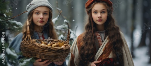 Teen and little girl in winter forest with basket of branches and berries. Medieval peasant sisters with firewood. Christmas-themed photoshoot